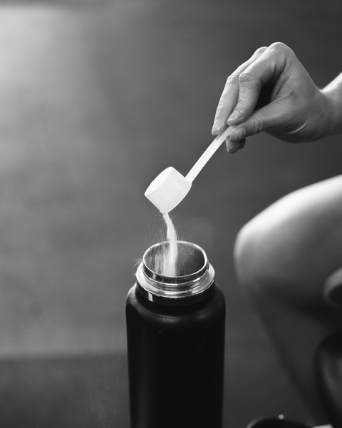 A close-up, high-contrast shot of a protein powder scoop being poured into a shaker bottle, emphasizing the simplicity of the supplement routine.